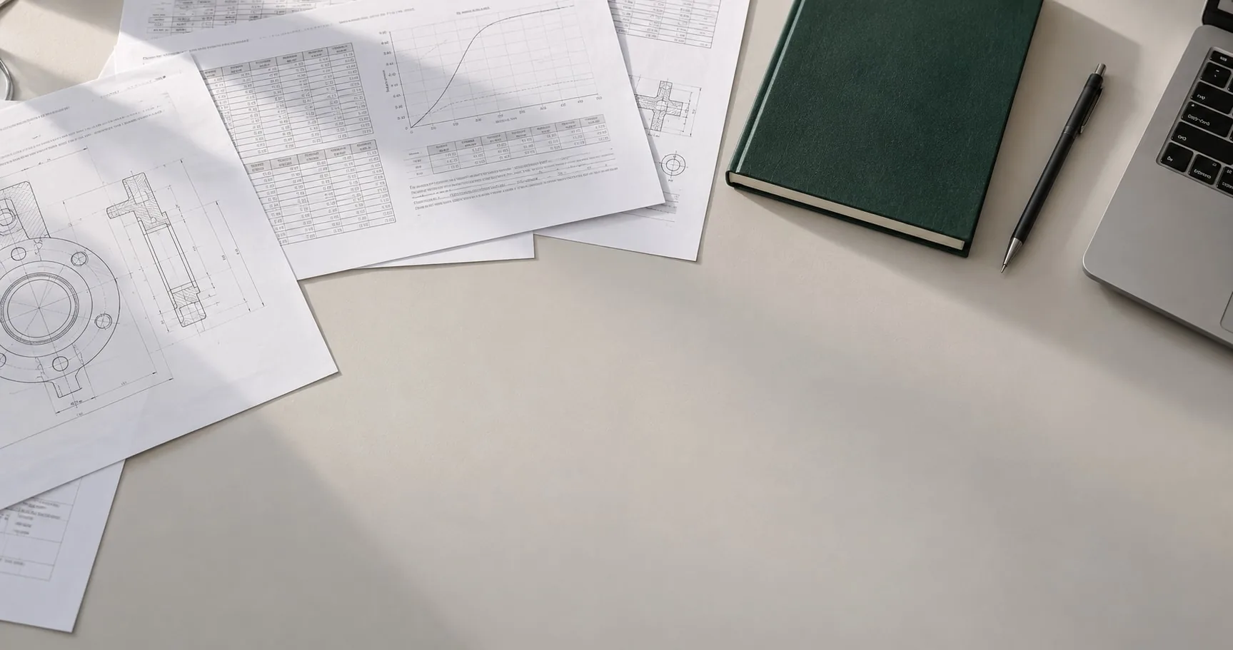 Engineering calculation sheets, a notebook and a laptop on a desk